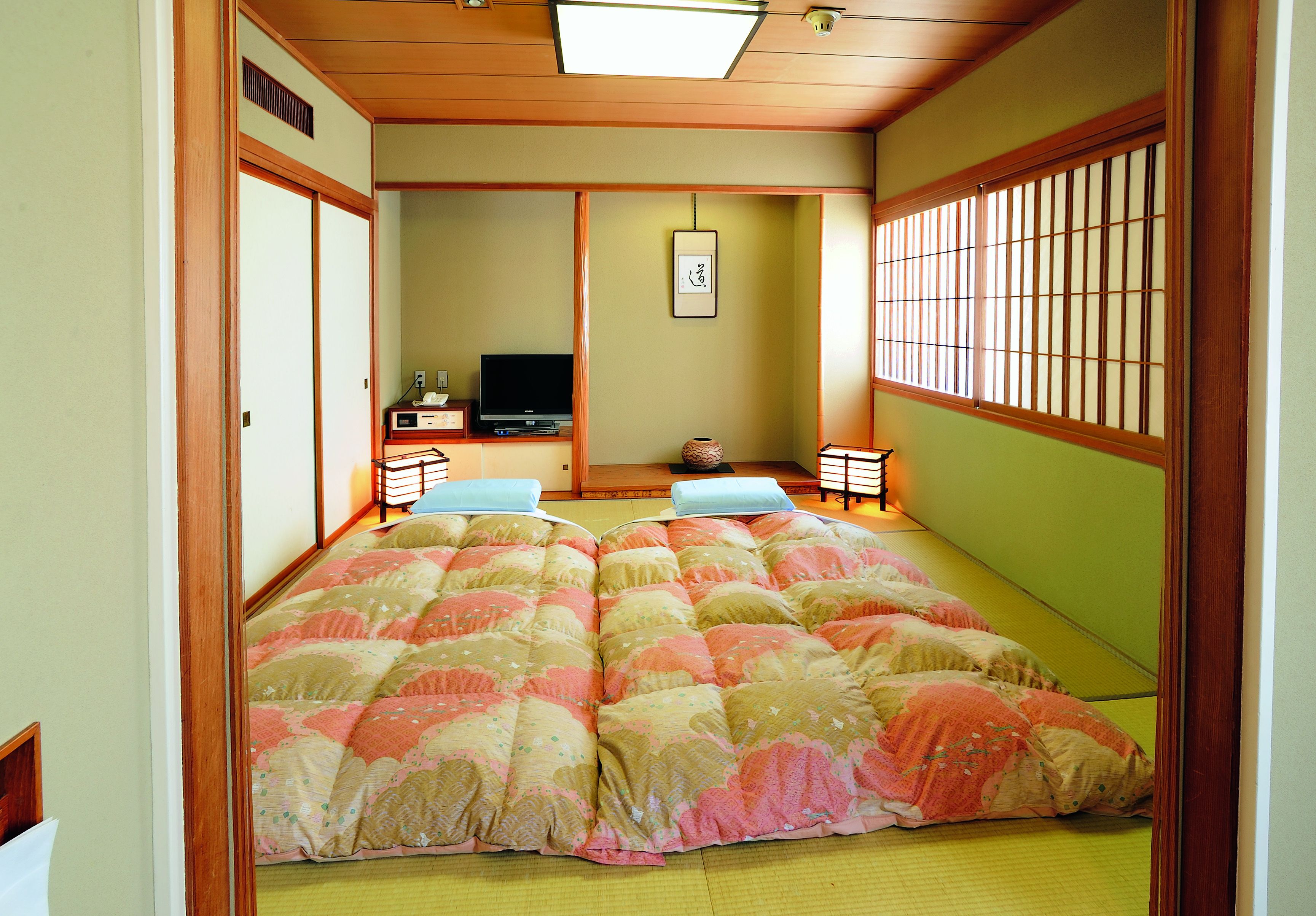 Quarto japonês tradicional com tatames, futon, televisão e um painel shoji.