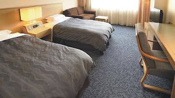 Ein Hotelzimmer mit zwei Betten, einem Schreibtisch, einem Sessel, einem Fernseher und einem Fenster mit Vorhängen.