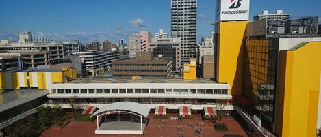 A modern building with a yellow and white facade, a large open plaza with outdoor seating, and a prominent Bridgestone sign.