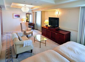 Una habitación de hotel con sofá, sillón y televisor sobre un mueble de madera.
