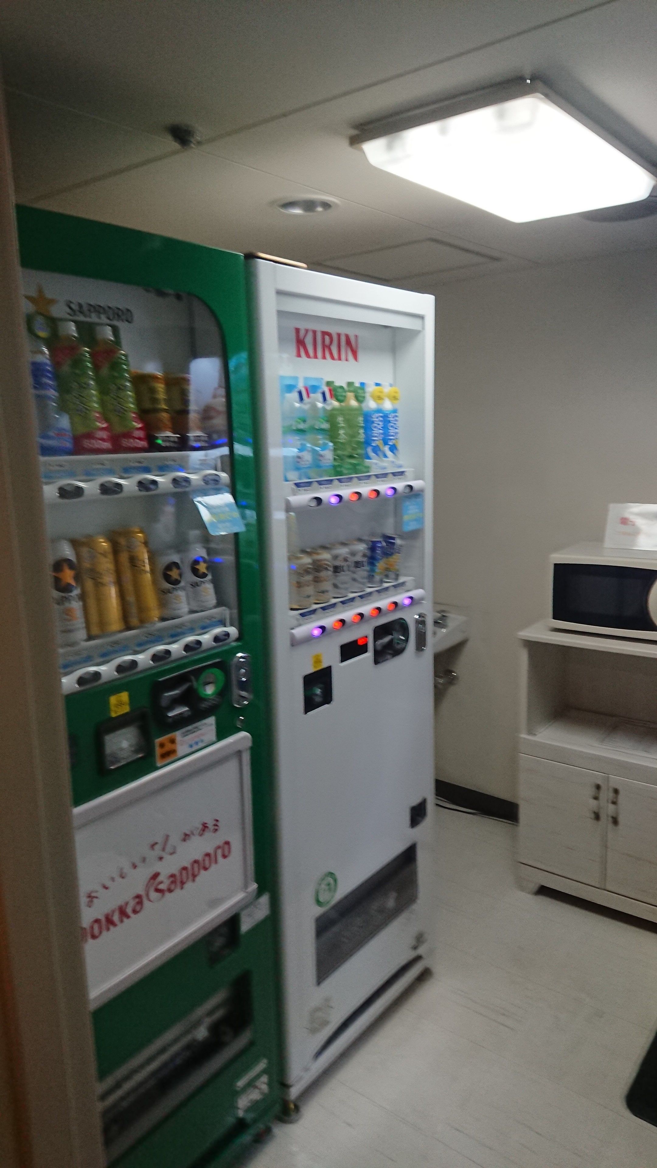 Ein Getränkeautomat mit grün-weißer Gestaltung, beschriftet mit 'KIRIN' und 'Sapporo'. Er enthält verschiedene Getränke und Snacks.