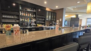 A bar area with a long counter, bar stools, shelves with bottles, and a television. - Holiday Inn Champaign by IHG (Champaign)