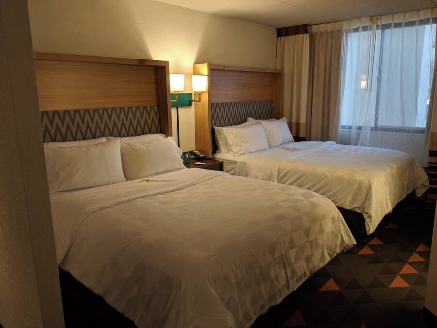 A hotel room with two beds, a nightstand with a phone, and a window with curtains.