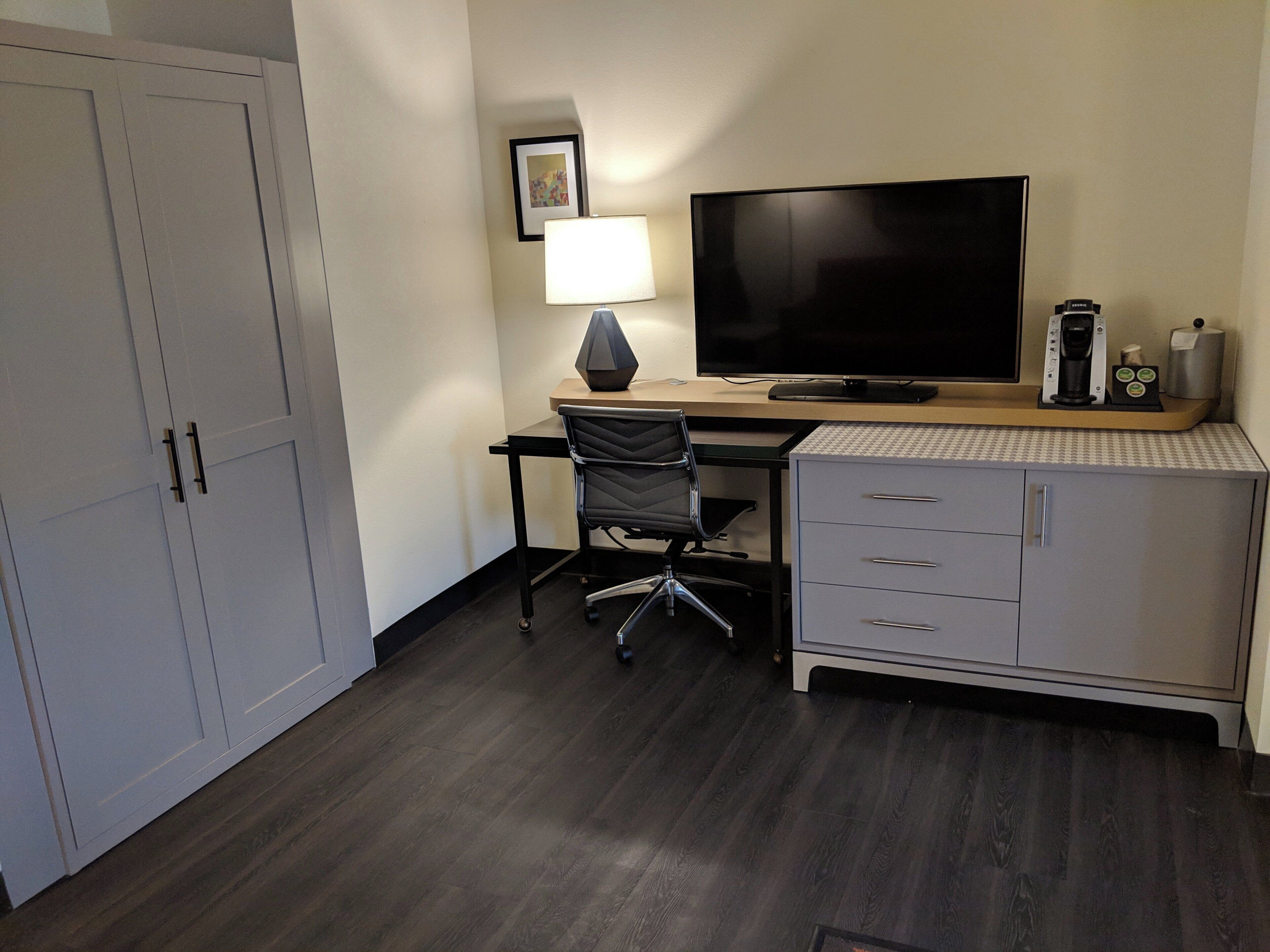 A hotel room with a desk, chair, television, lamp, and a minibar.