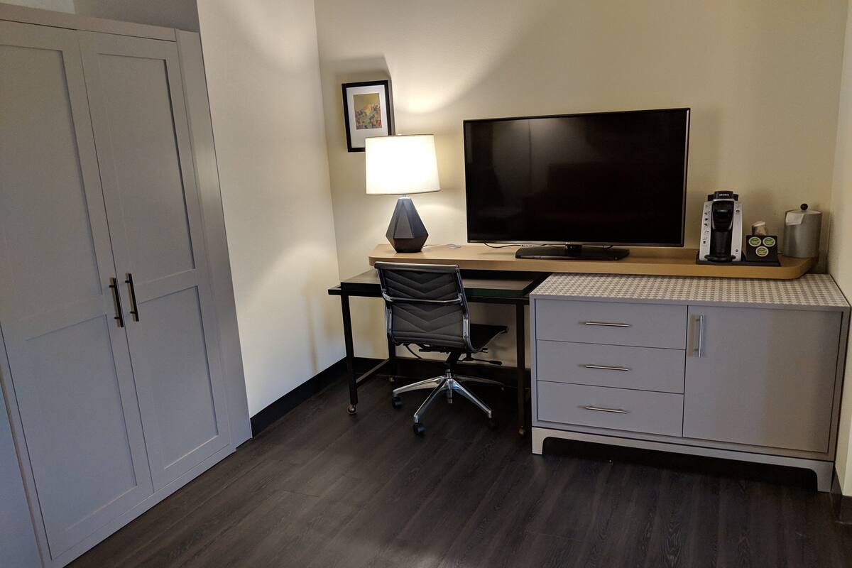 A hotel room with a desk, chair, TV, lamp, and a minibar.