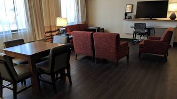 Een hotelkamer met een eettafel, vier stoelen, een zithoek, een televisie en een koffiezetapparaat.