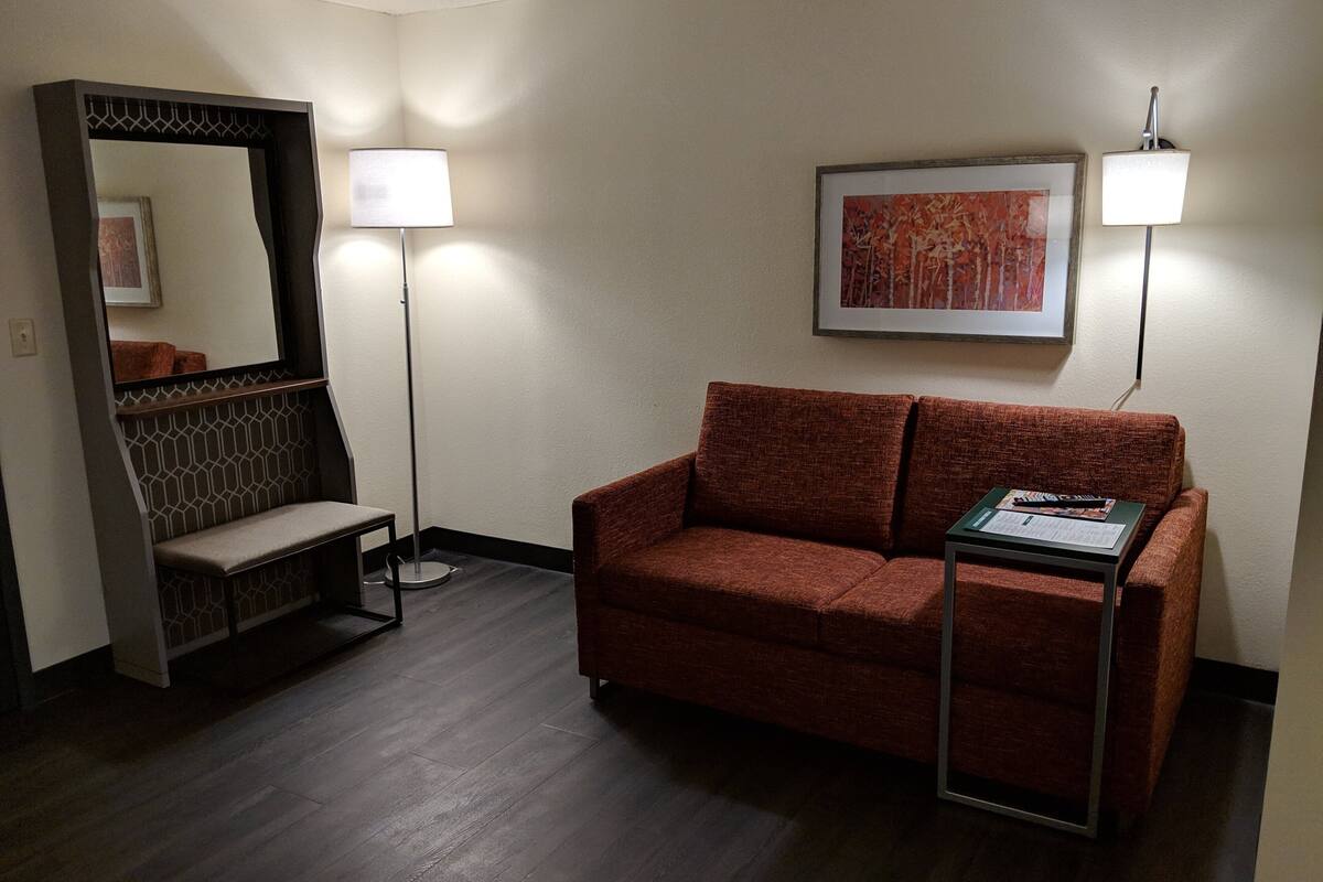 A room with a brown sofa, a bench, a framed picture on the wall, and two floor lamps.