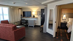 Ett hotellrum med en röd soffa, ett skrivbord med en dator, en tv och en säng med en mönstrad matta.