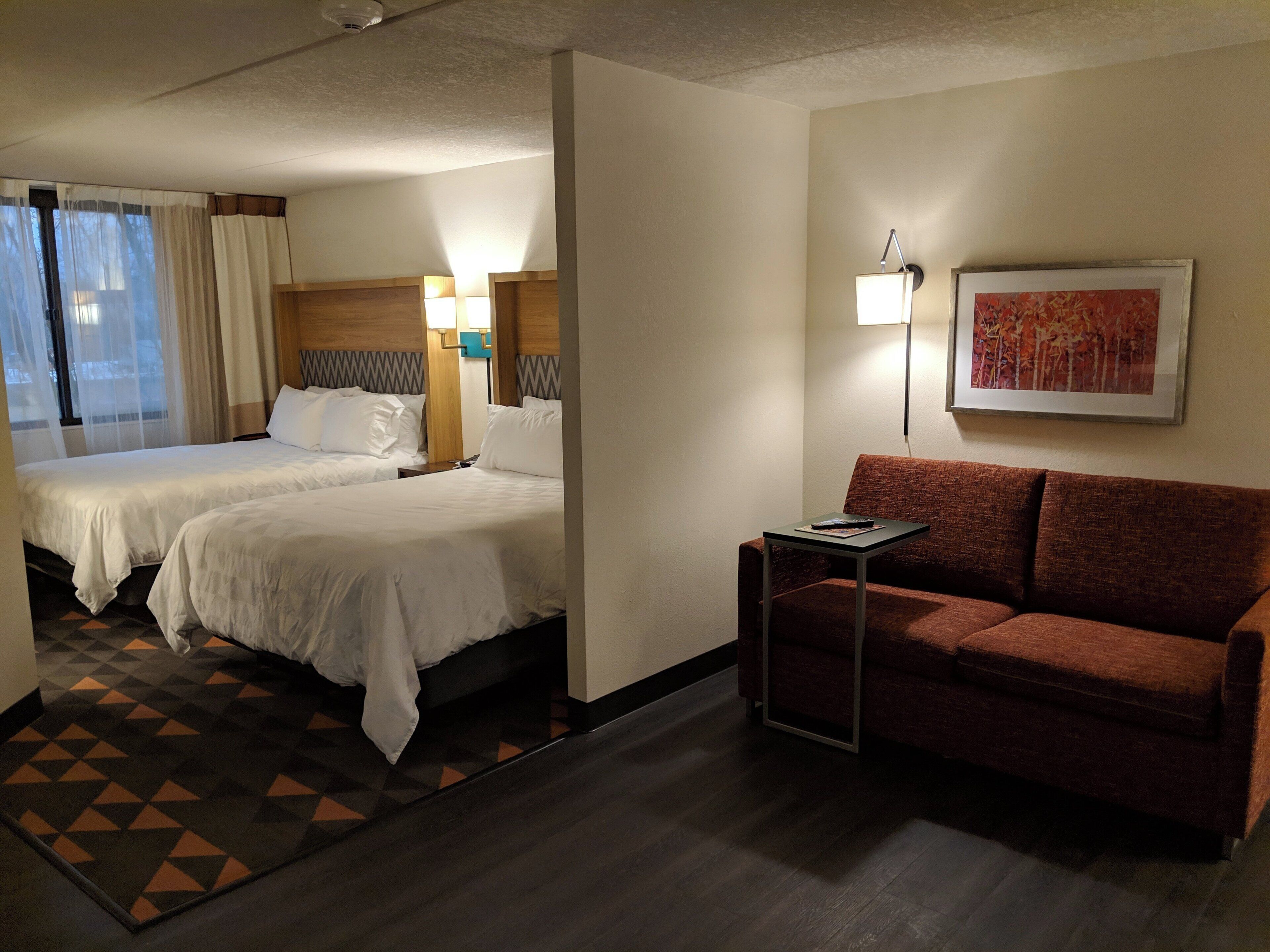 A hotel room with two beds, a sofa, a small table, and a painting on the wall.