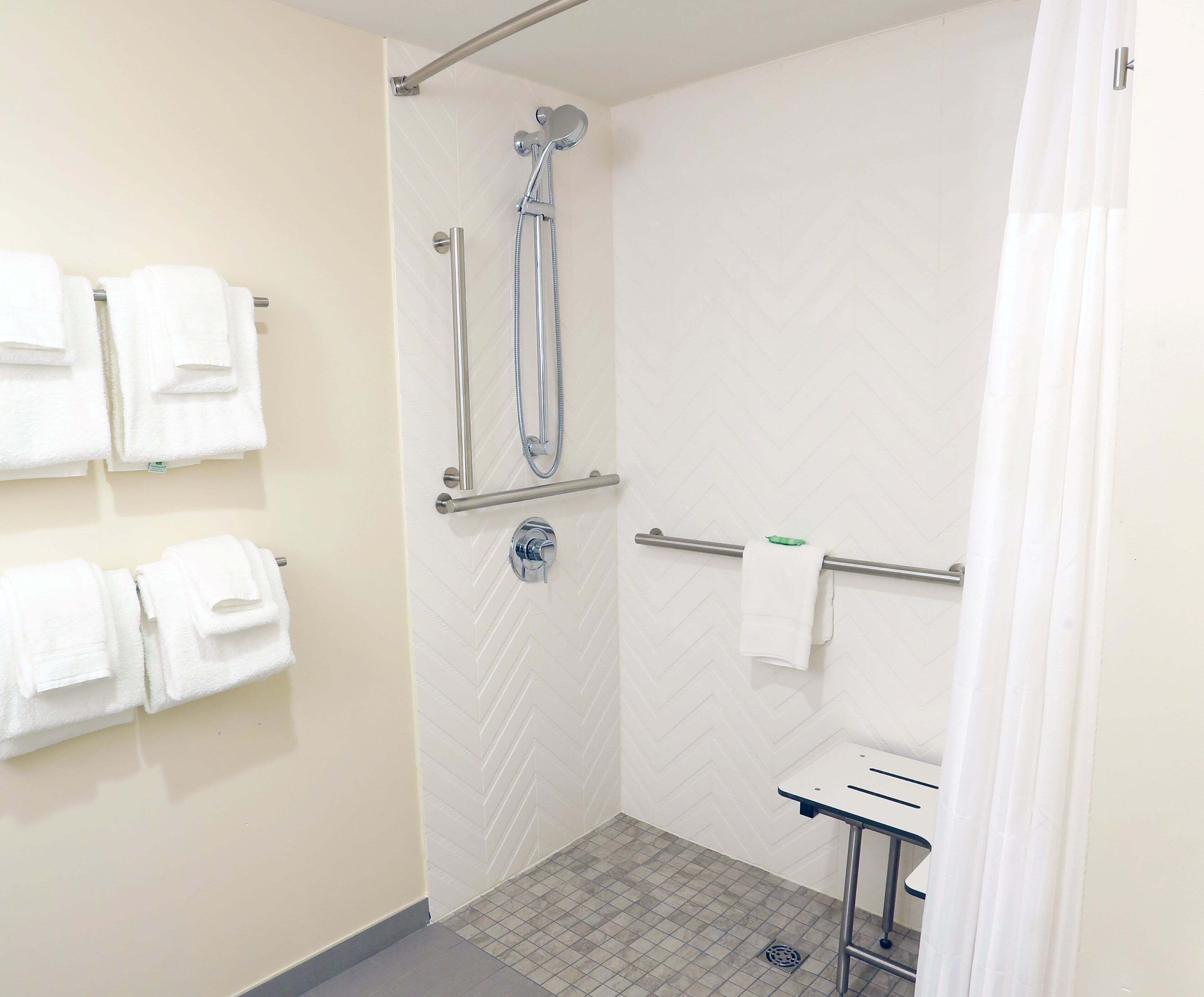 Un espace douche doté d’une porte en verre, d’un porte-serviettes avec des serviettes pliées et d’un petit lavabo avec un miroir.
