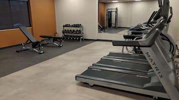 Un gimnasio con cintas de correr, mancuernas y bancos de pesas.