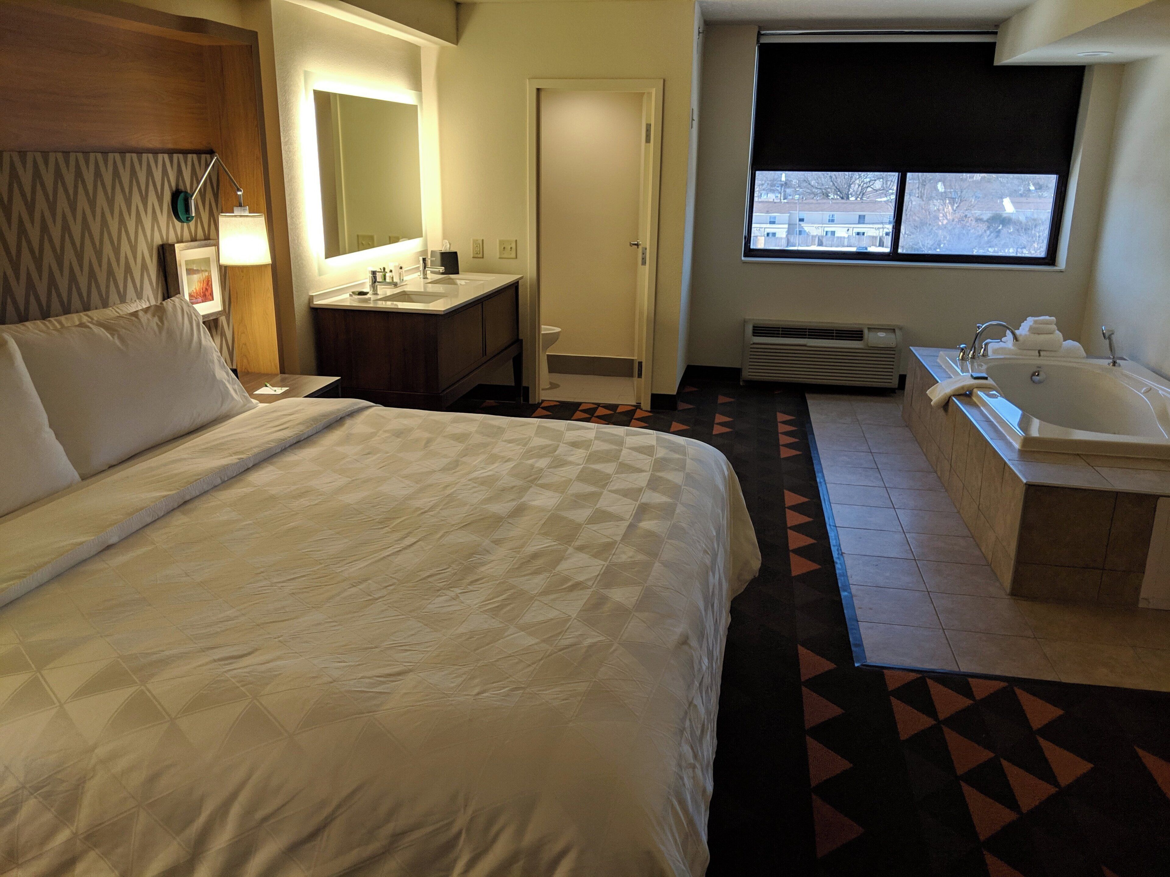 A hotel room with a large bed, a bathroom with a bathtub, a sink, and a window with a view.