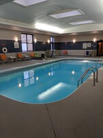 Una piscina interior con silla de salvavidas, sillas de descanso y un elevador de piscina.