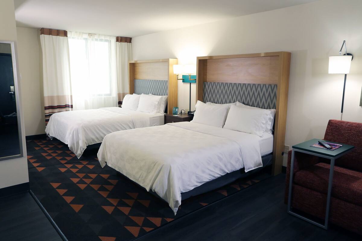 A hotel room with two beds, a desk, a chair, and a lamp.