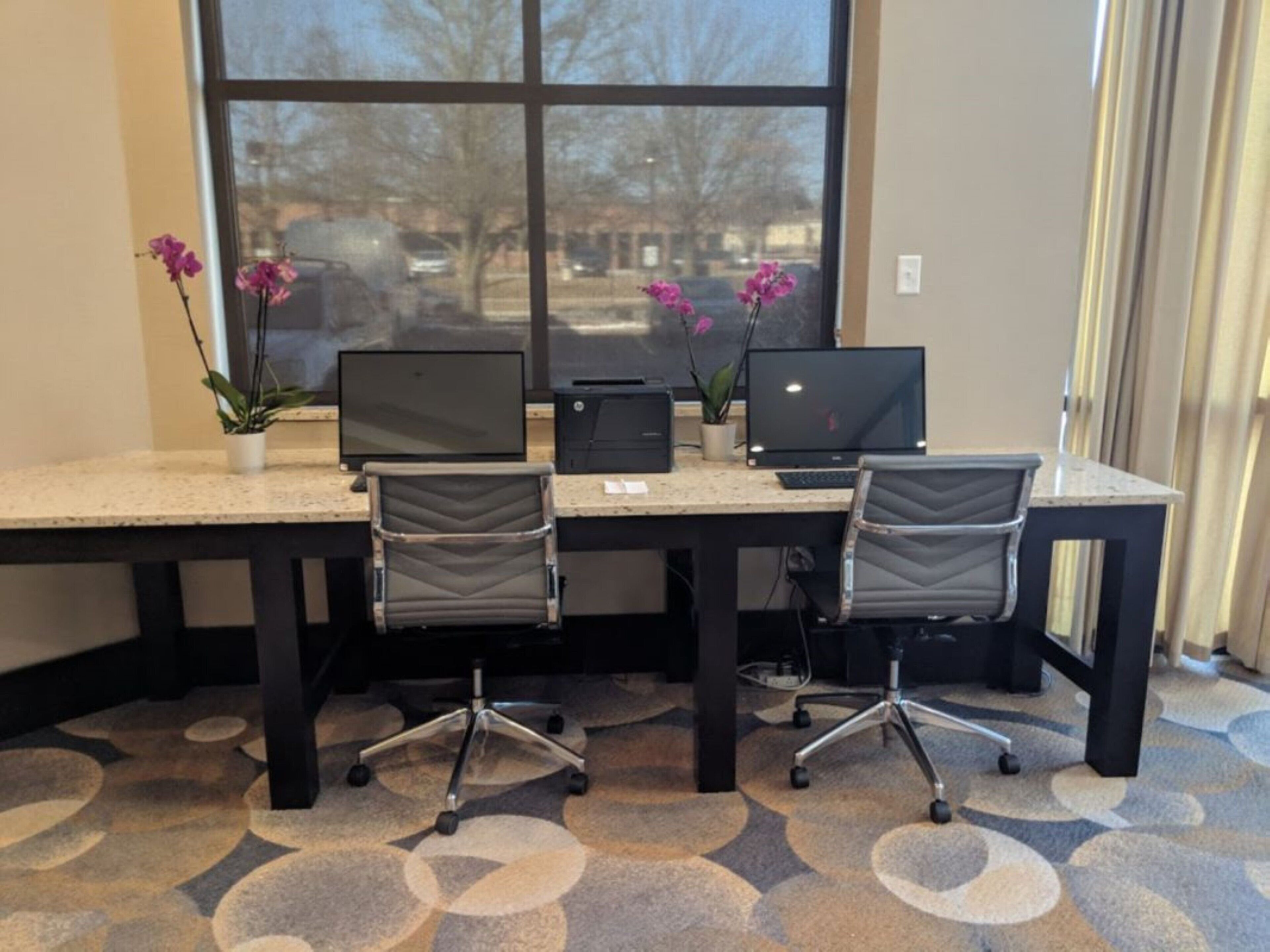 A workspace with two desks, each with a computer and a printer, and two office chairs.