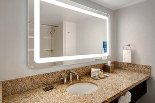 Un baño con encimera de granito, un lavabo blanco, un espejo con luz y un perchero para toallas.