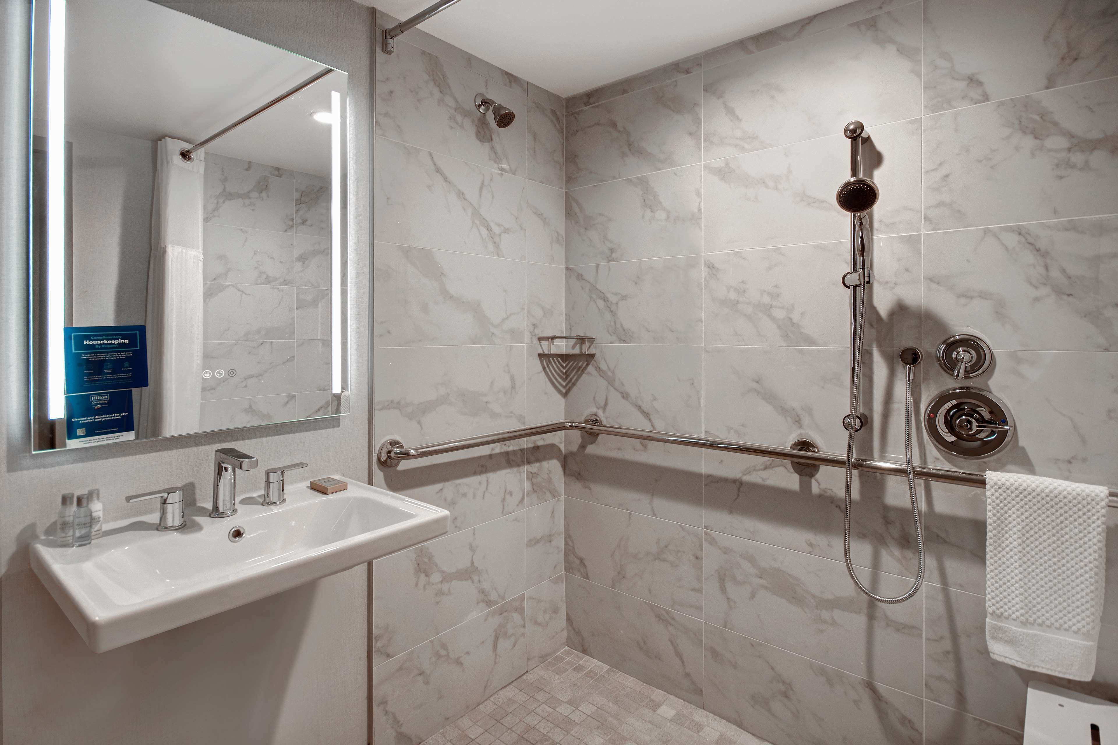 A bathroom with a white sink, a mirror, a shower with a handheld showerhead, and a grab bar.