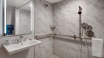 A bathroom with a white sink, a mirror, a shower with a handheld showerhead, and a grab bar.