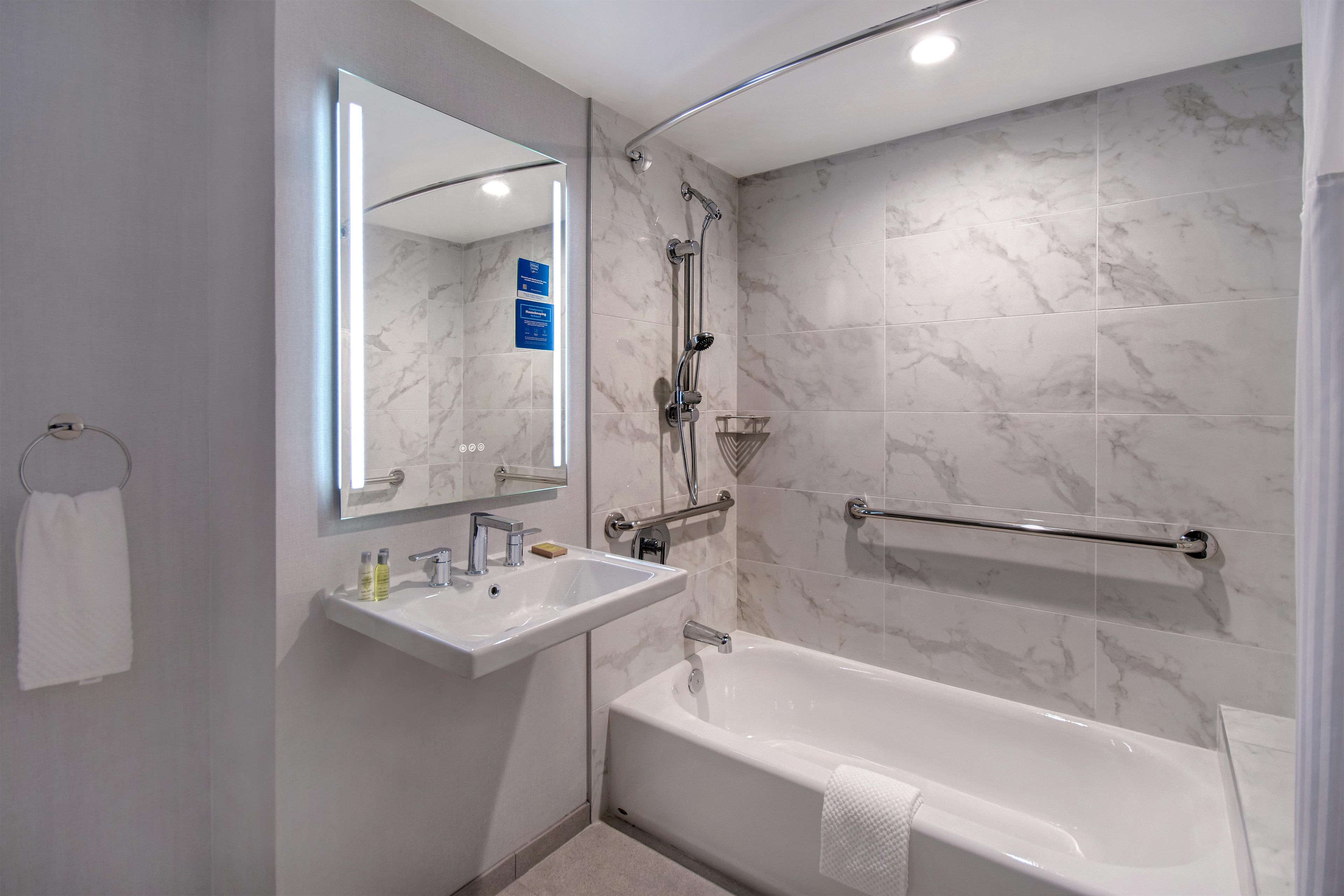 A modern bathroom with a bathtub, a sink, a shower, and a handrail.