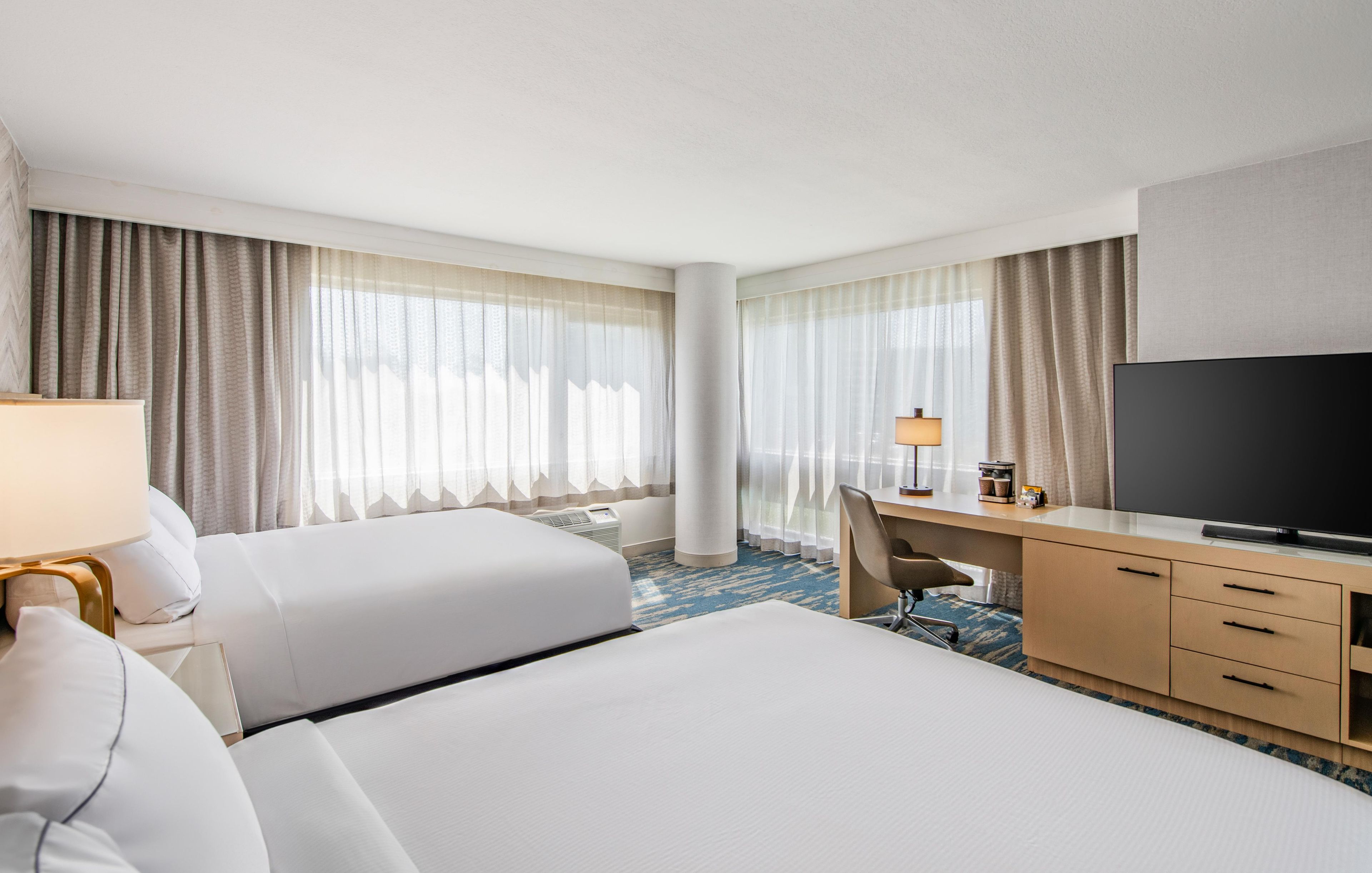 A hotel room with two beds, a desk, a television, and a window with curtains.
