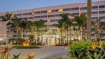 A hotel with a modern facade, palm trees, and a well-maintained garden.
