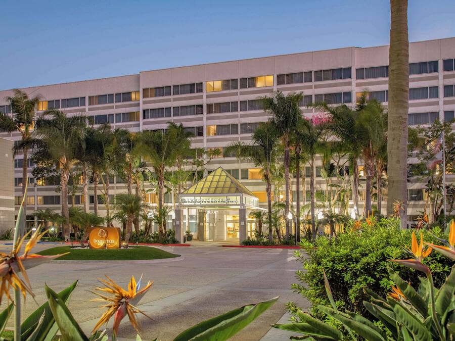 A hotel with a modern design, featuring a central courtyard with palm trees and a well-lit entrance.