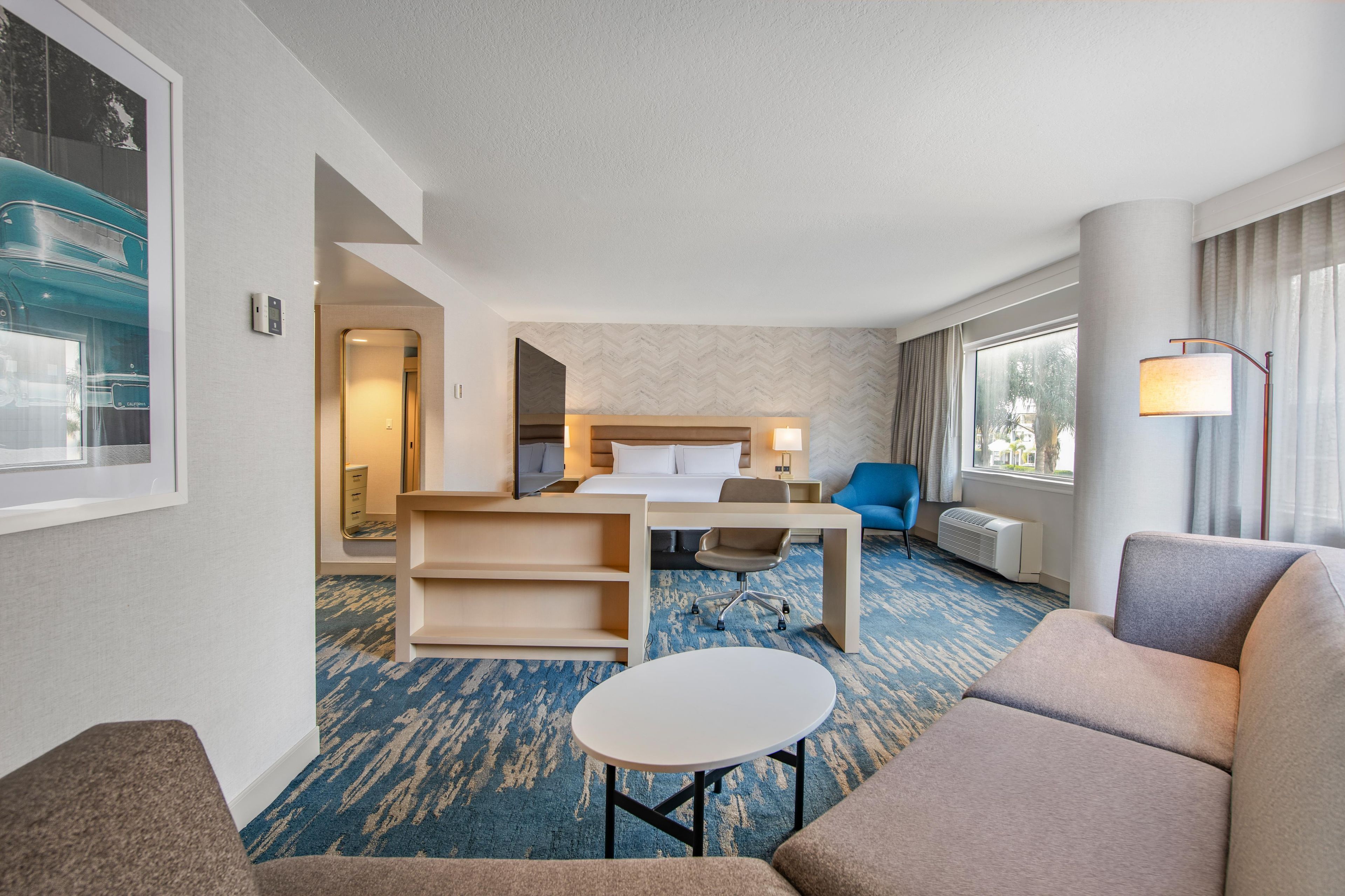 Una habitación de hotel con cama, escritorio, silla, mesita y sofá.