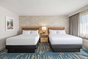 Una habitación de hotel con dos camas, una mesita de noche con lámpara, un papel tapiz de diseño espiga y un cuadro en la pared.