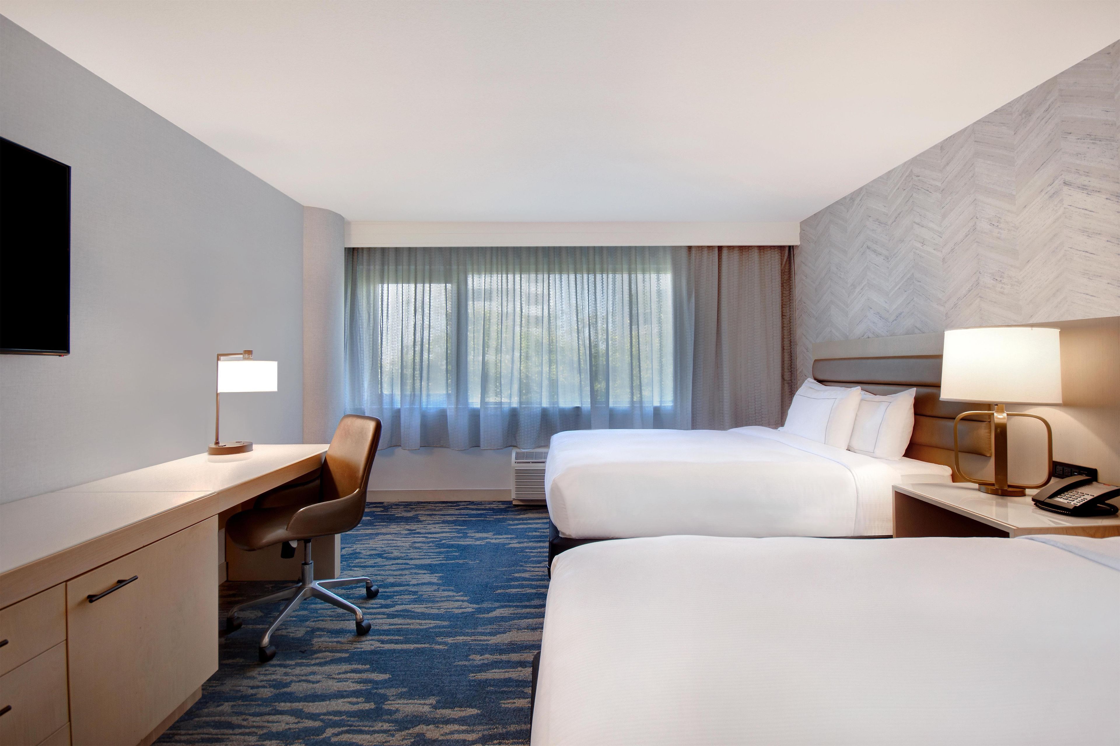 Une chambre d’hôtel avec deux lits, un bureau, une chaise, une lampe et un téléviseur.
