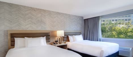 A hotel room with two beds, a herringbone-patterned wall, a large window with a view, and a blue carpet.
