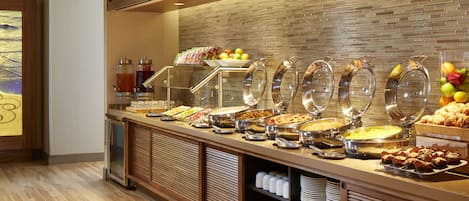 A buffet area with various food items and beverages, including fruits, salads, and desserts.