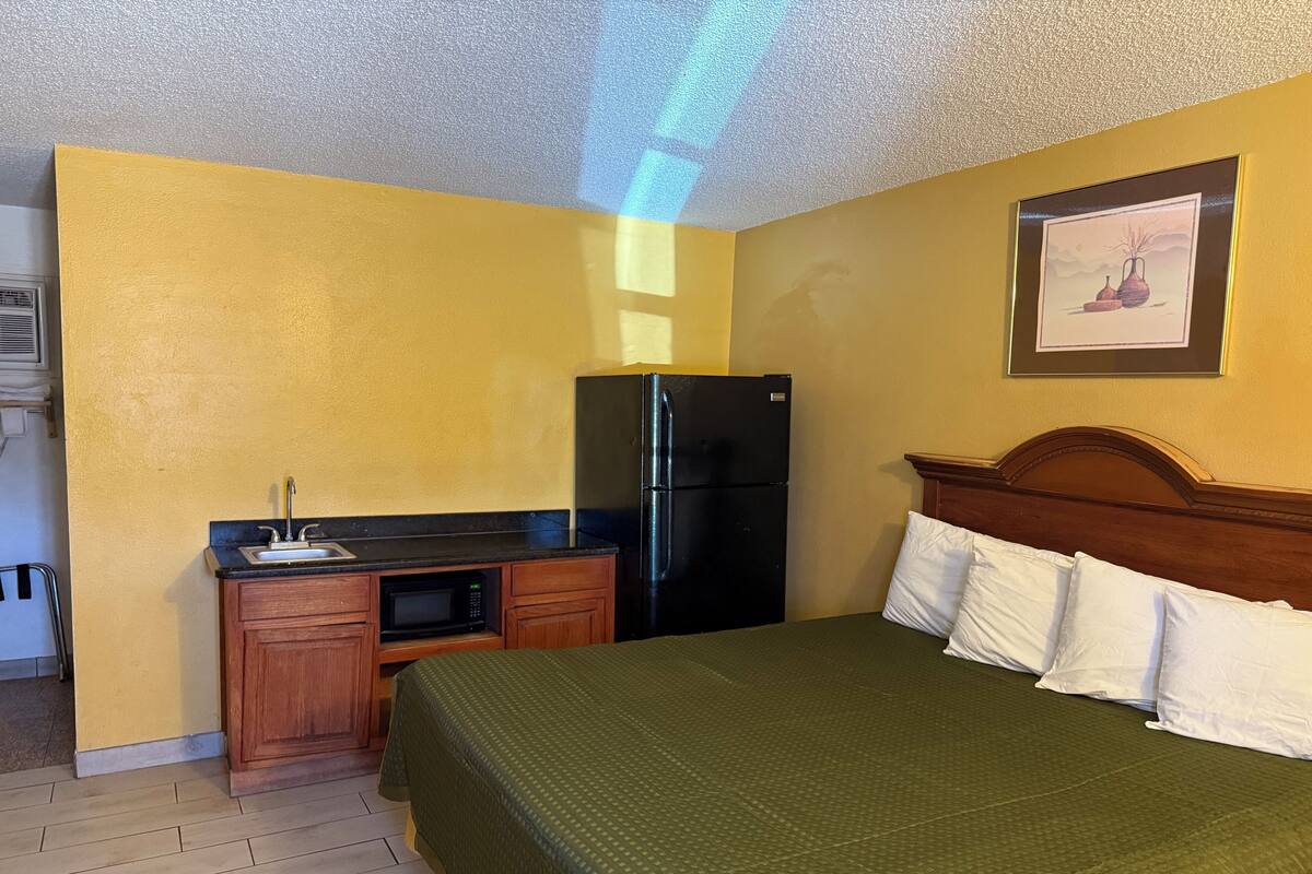 A hotel room with a bed, a small kitchenette, and a refrigerator.