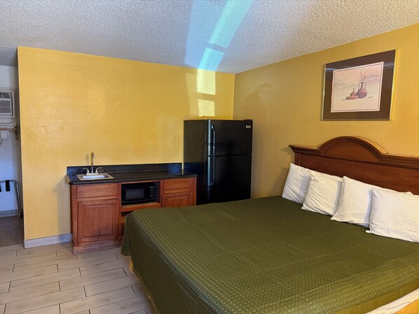A hotel room with a bed, a small kitchenette, and a refrigerator. - La Vista Inn (Clovis)