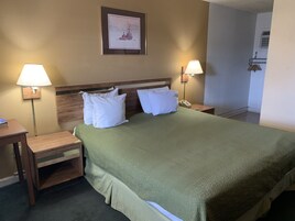 Una habitación de hotel con una cama grande, dos mesitas de noche, dos lámparas, un cuadro enmarcado en la pared y una mesita de madera.