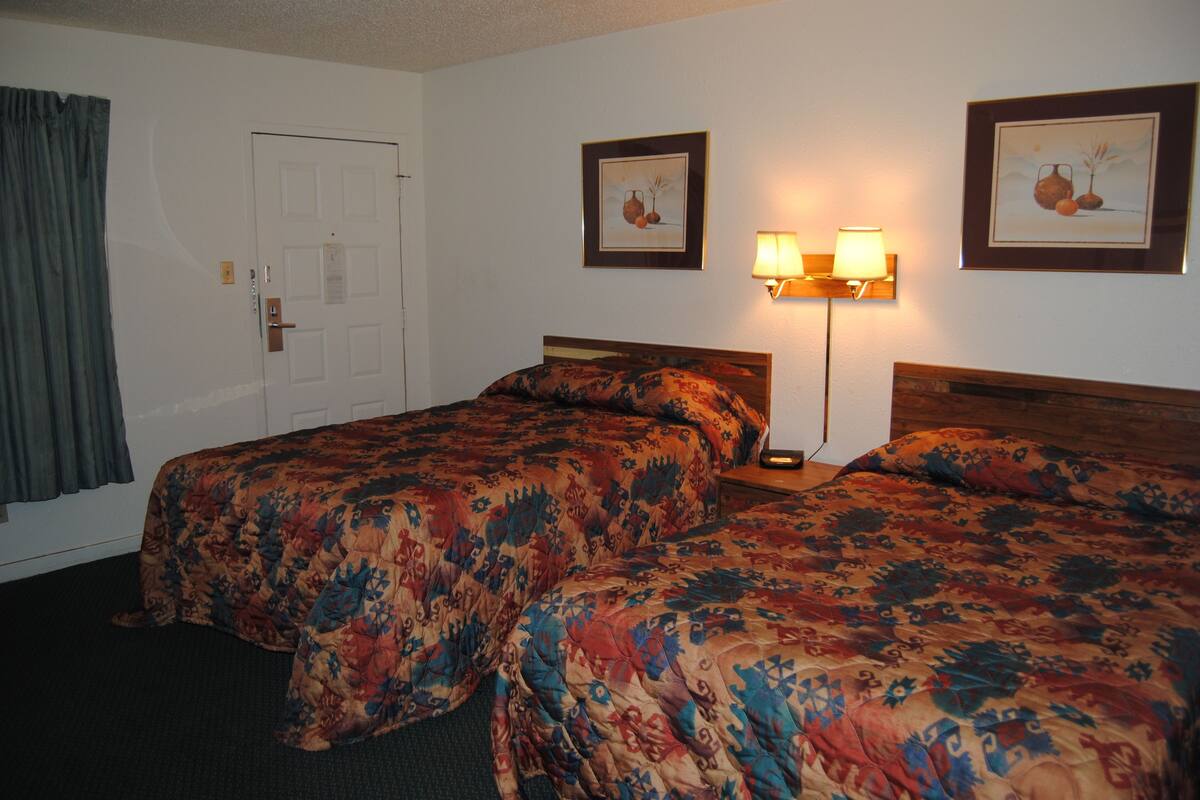 A hotel room with two beds, a door, a lamp, and two framed pictures on the wall.