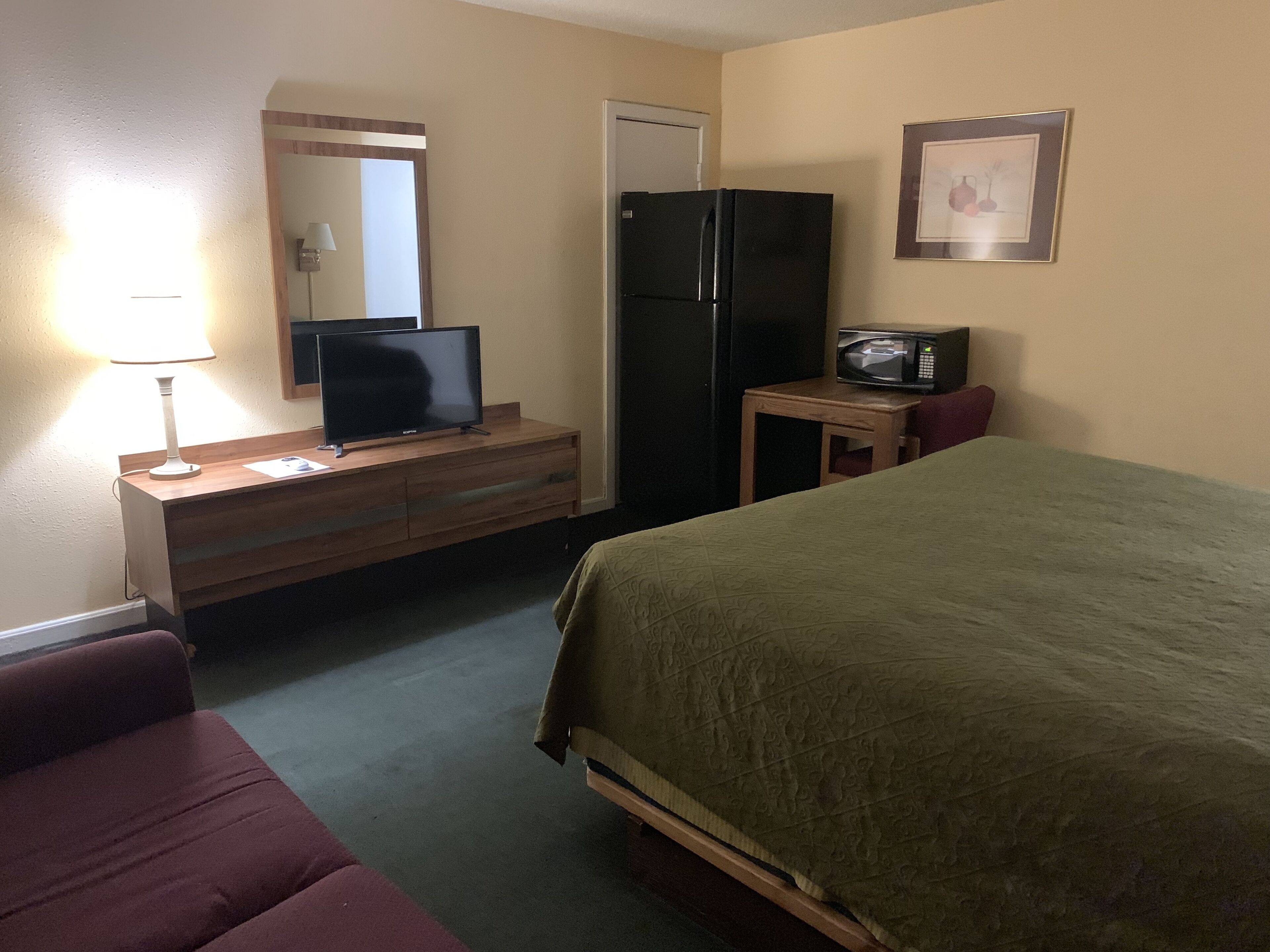A hotel room with a bed, a desk with a television, a refrigerator, a microwave, and a small table.
