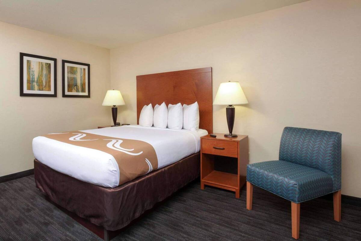A hotel room with a bed, two bedside lamps, a chair, and two framed pictures on the wall.