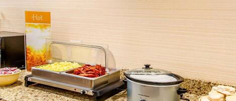 A buffet setup with various food items and a slow cooker on a granite countertop.