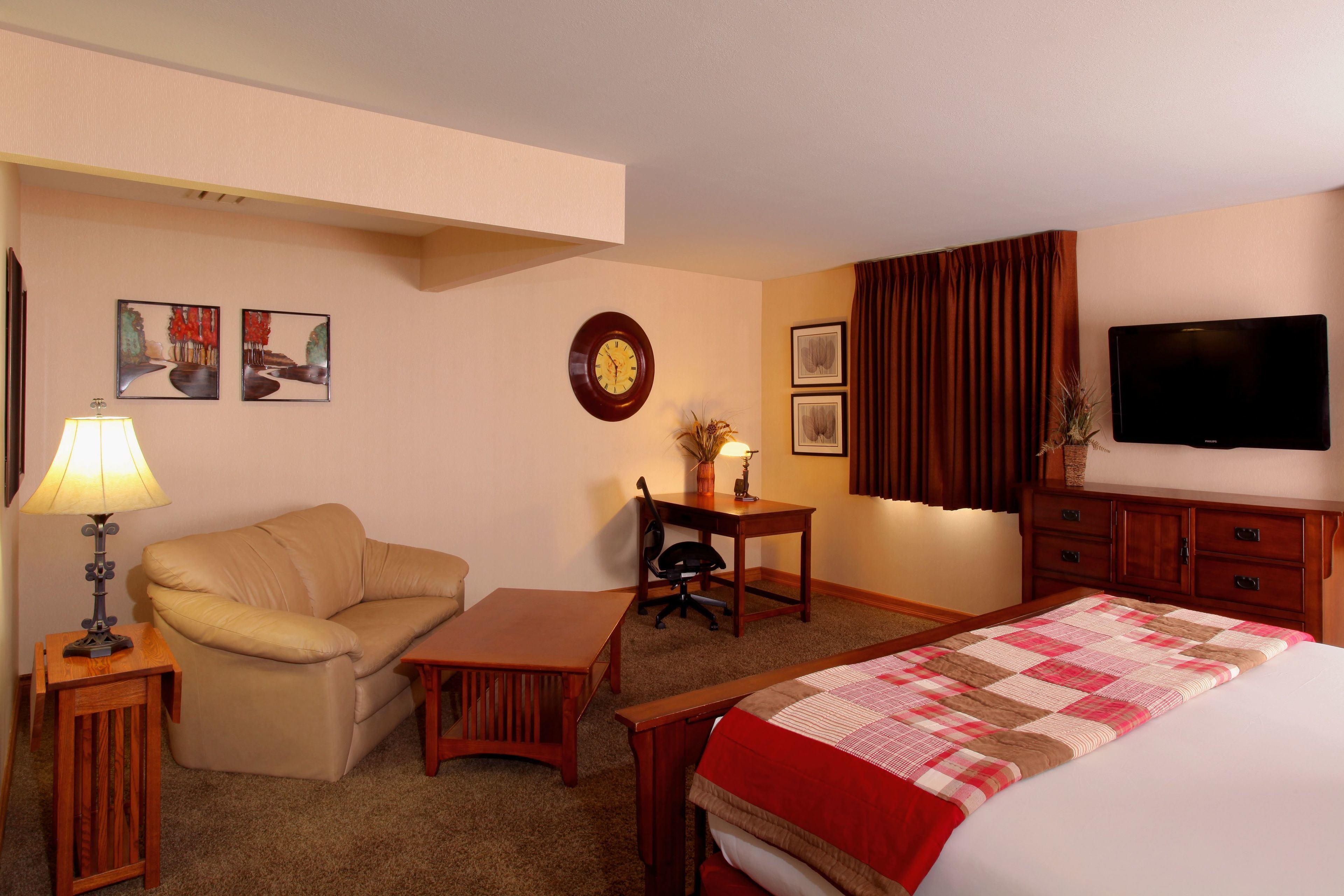 A hotel room with a bed, a desk, a chair, a sofa, a lamp, and a flat-screen TV.