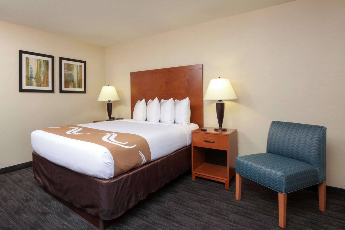 A hotel room with a large bed, two bedside tables with lamps, a chair, and two framed pictures on the wall.
