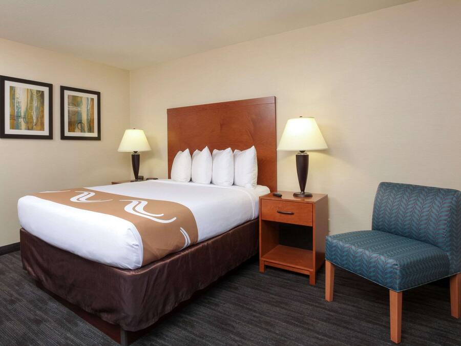 A hotel room with a large bed, two bedside tables with lamps, a chair, and two framed pictures on the wall.