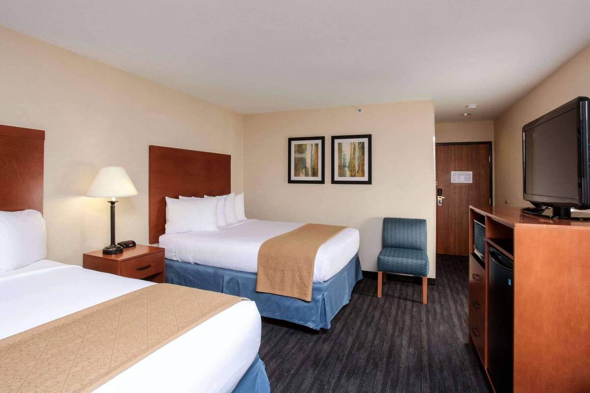 A hotel room with two beds, a desk, a chair, a television, and artwork on the wall.