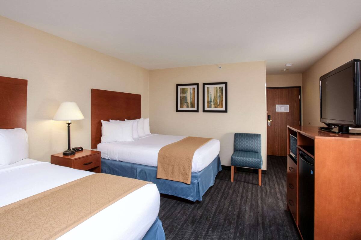 A hotel room with two beds, a desk with a television, a chair, and artwork on the wall.