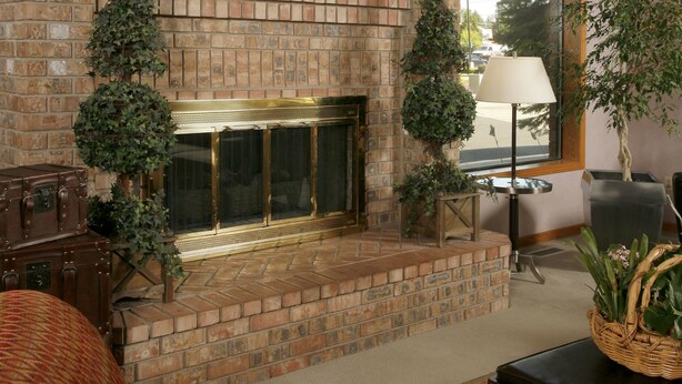 A brick fireplace with a decorative plaque, a large window with a view of the outside, and a patterned sofa in a living area. - Quality Inn Oakwood (Spokane)
