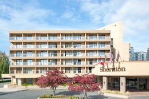 A Sheraton hotel with multiple floors, balconies, and a parking lot with red-leaved trees. - Sheraton Vancouver Airport Hotel (Richmond)