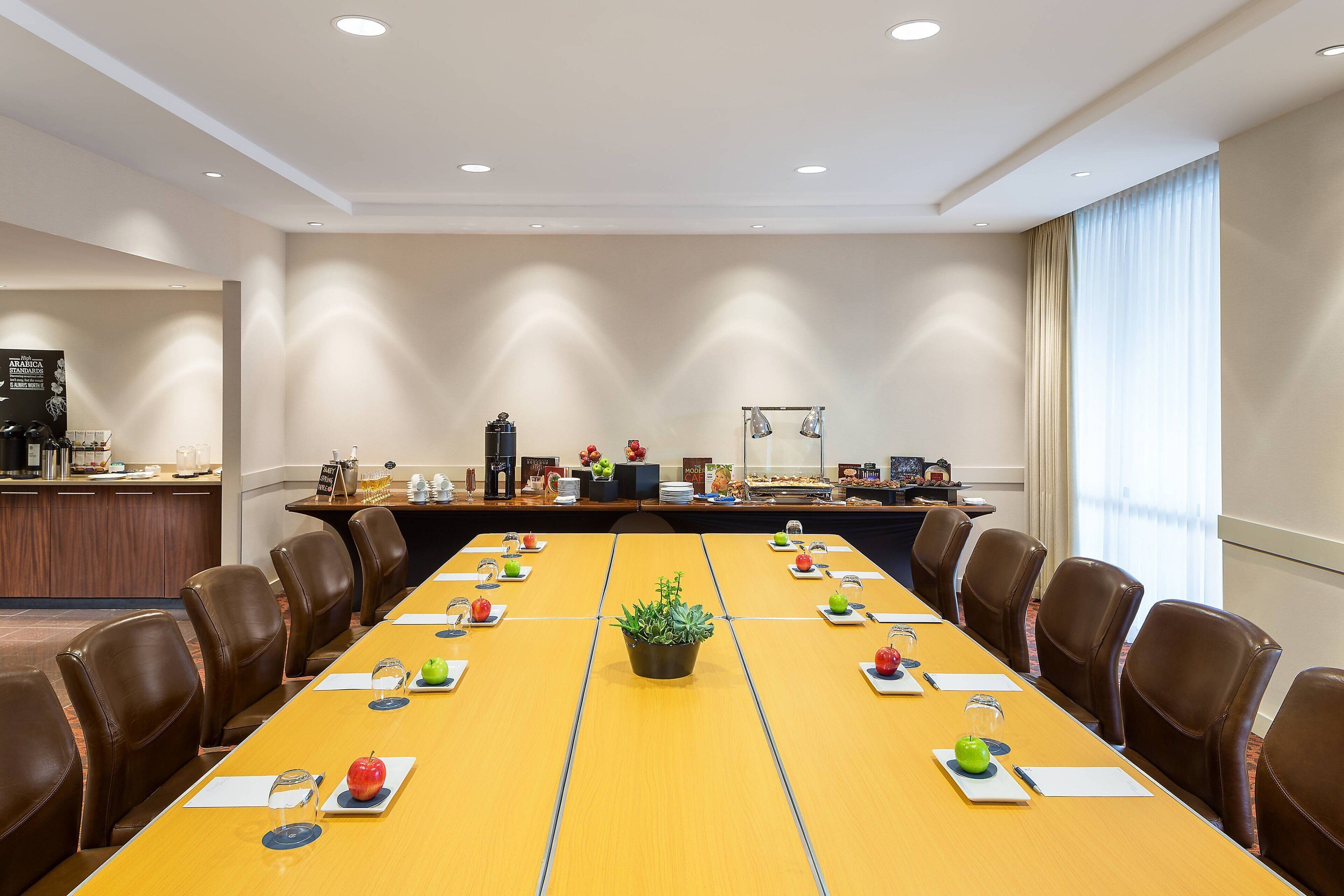 A conference room with a long table, brown leather chairs, and a potted plant in the center.