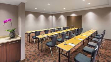 Un salón de conferencias con largas mesas, sillas y una orquídea en maceta.