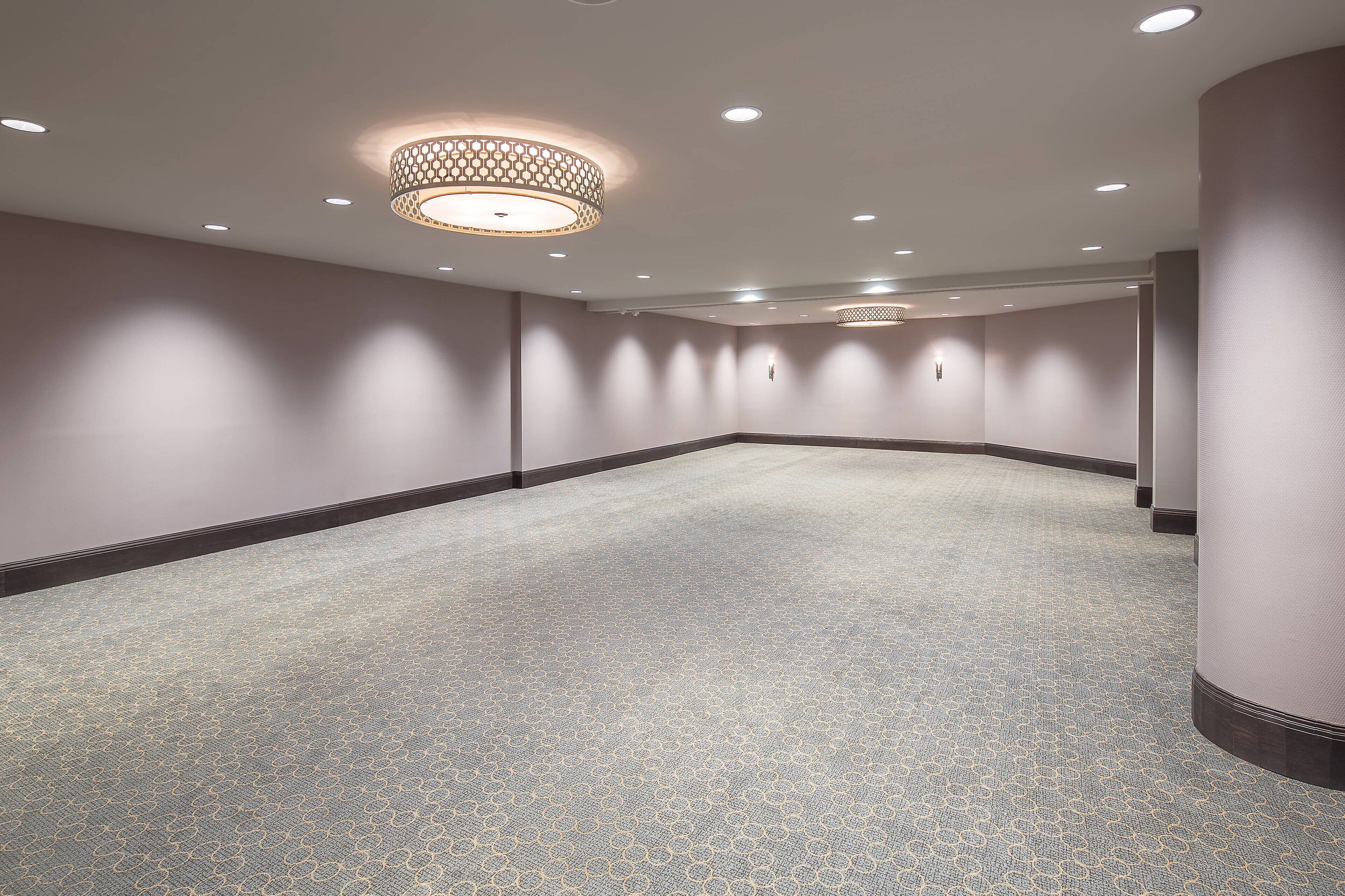 A spacious, carpeted hallway with recessed lighting and a patterned floor.