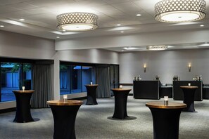 Un hall d’hôtel avec des tables rondes, un coin bar et de grandes fenêtres.