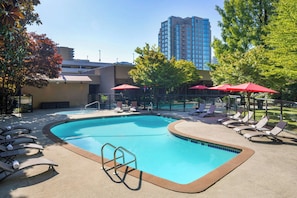 A swimming pool with lounge chairs and umbrellas, surrounded by trees and a tall building in the background. - Sheraton Vancouver Airport Hotel (Richmond)